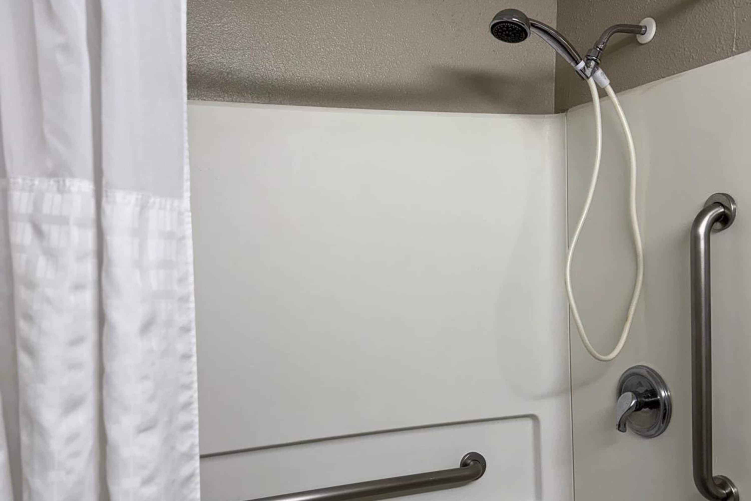 Zona de ducha con cabezal de ducha de mano, control de ducha manual y barra de apoyo.