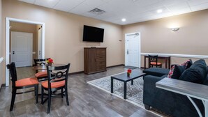 A living room with a dining area, a flat-screen TV mounted on the wall, and a sofa with a coffee table. - Travelodge by Wyndham Lakeland (Lakeland)