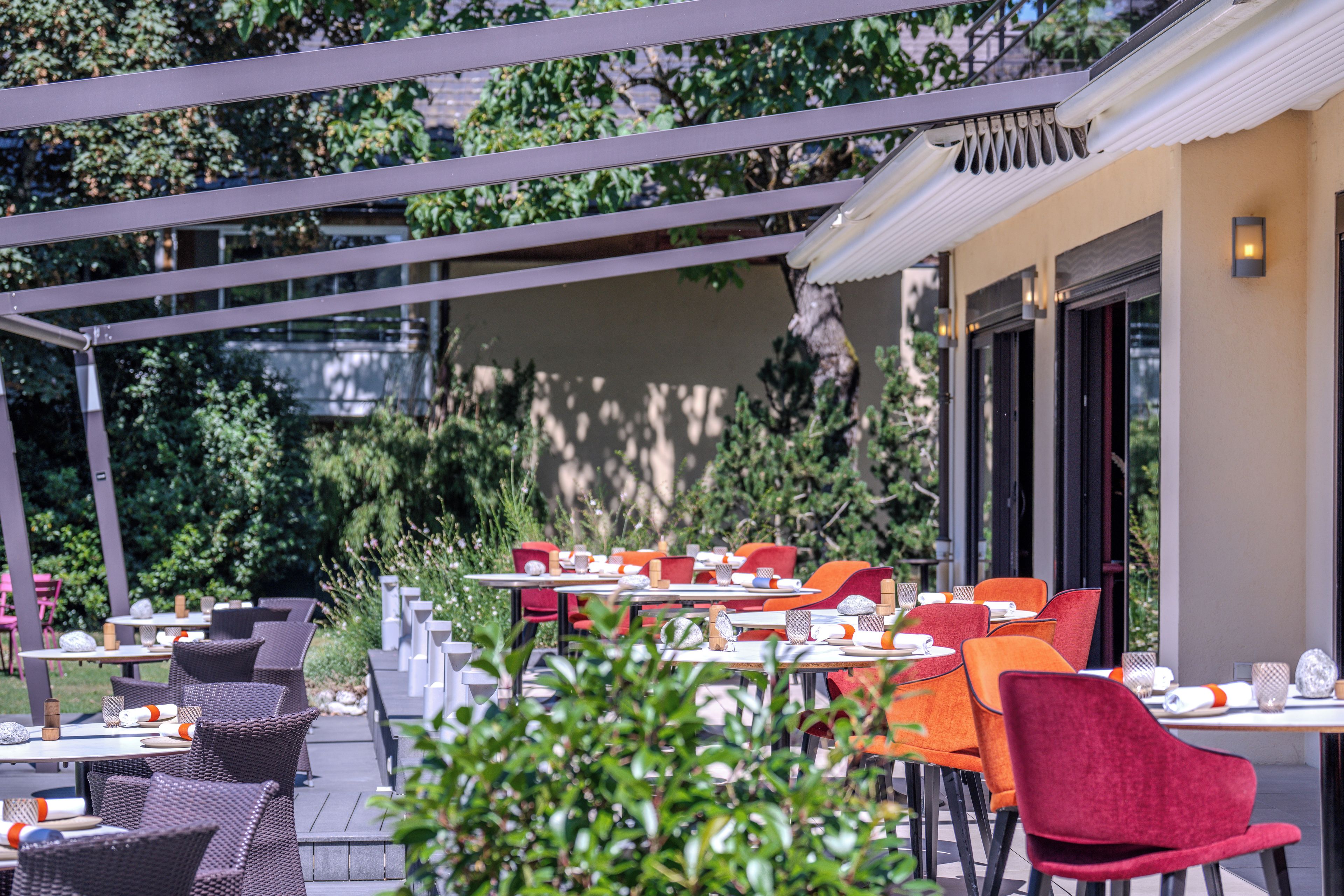 An outdoor dining area with tables and chairs, surrounded by greenery.