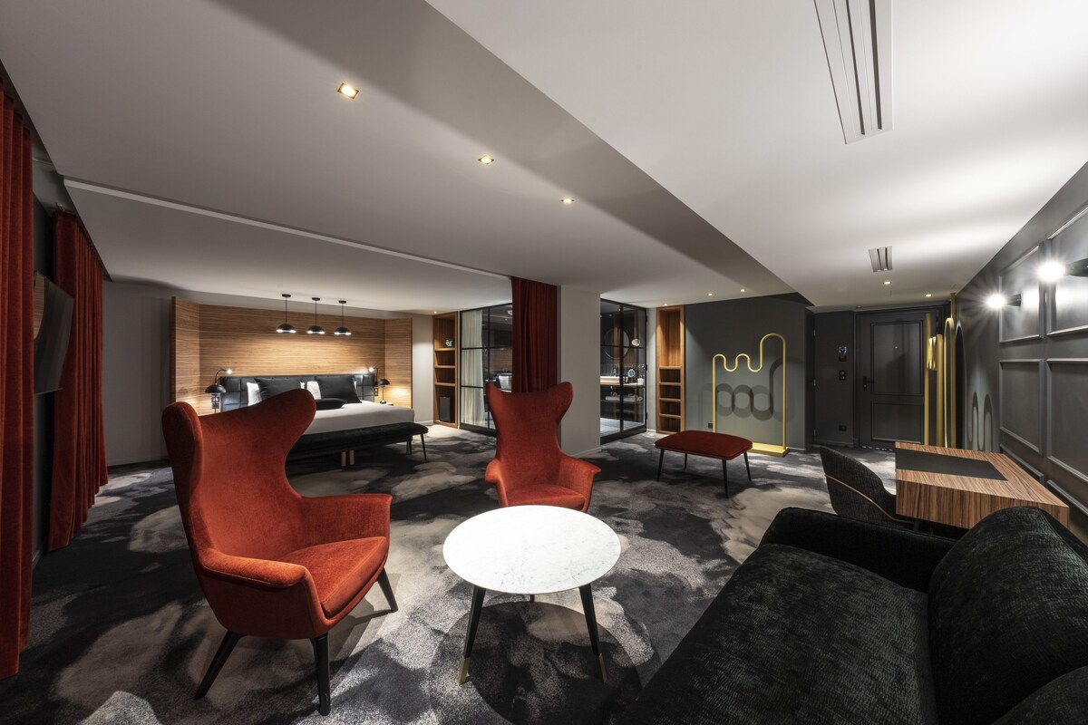 A modern hotel lobby with a sofa, chairs, a round table, and a bar area.