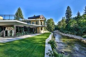 A modern two-story house with a glass facade, a stone foundation, and a well-maintained lawn.