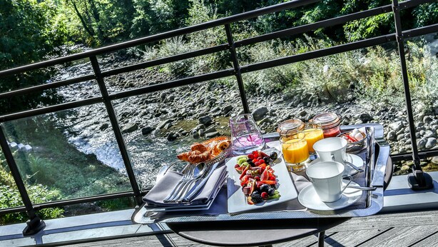 Een ontbijt met uitzicht op een rivier, inclusief een dienblad met fruit, sap en een croissant.