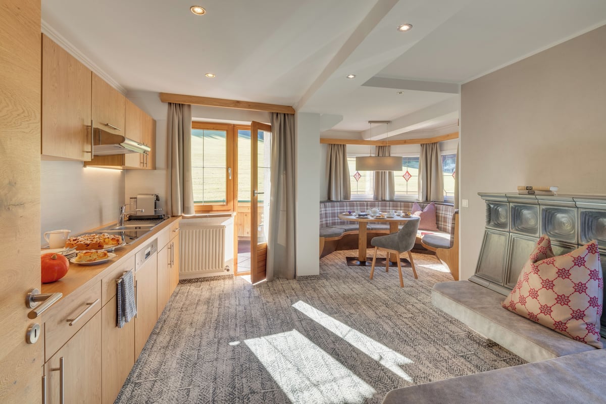 Una cocina moderna con armarios de madera, un comedor con mesa y sillas, y una zona de estar acogedora con sofá y cojines.