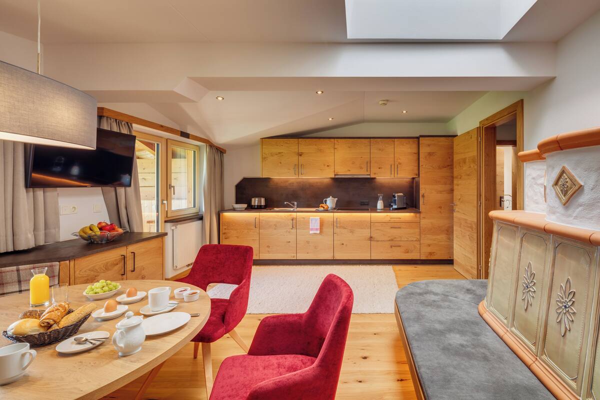 Una cocina moderna con armarios de madera, un comedor con sillas rojas y una zona para desayunar.