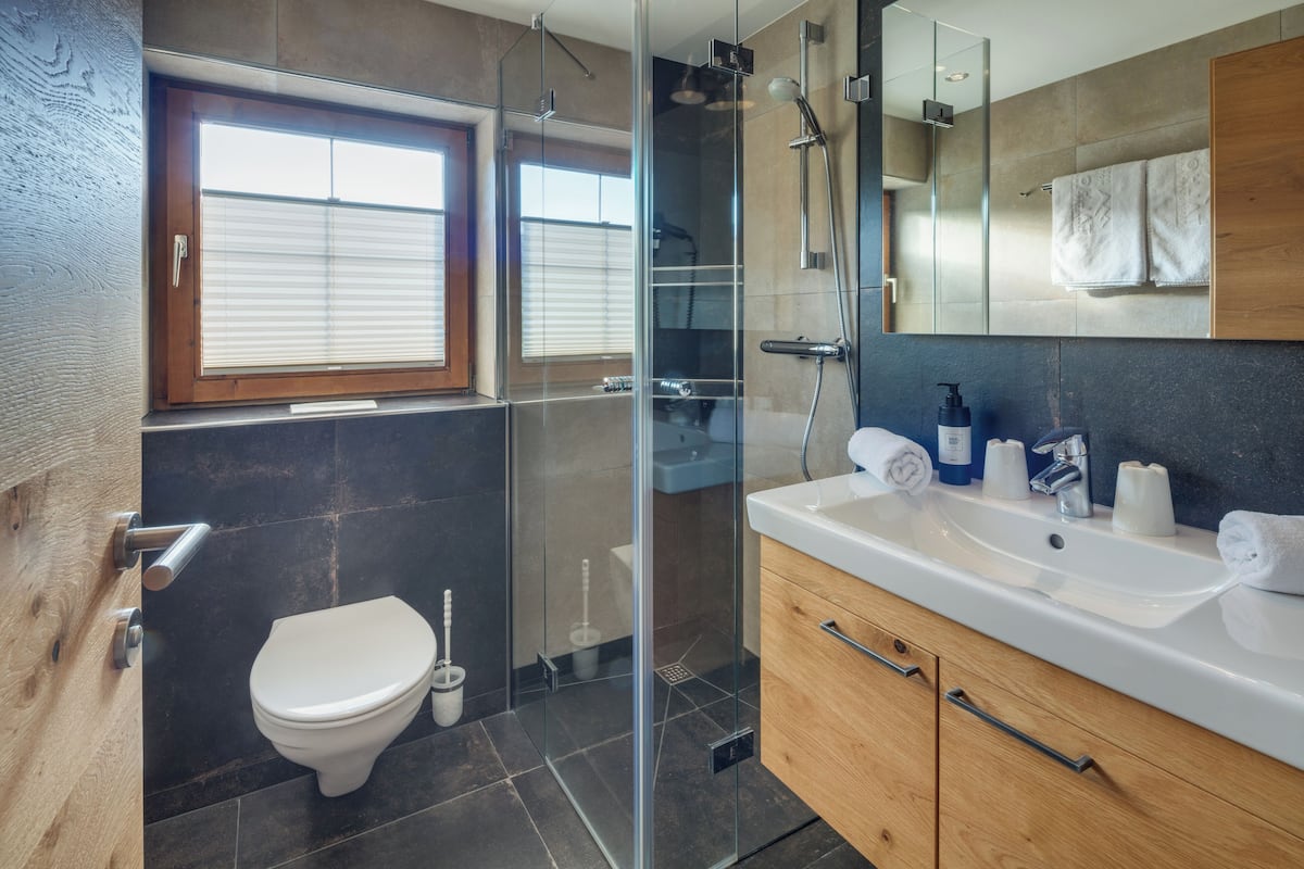 Un baño moderno con cabina de ducha de vidrio, inodoro blanco y tocador de madera con lavamanos y perchero para toallas.
