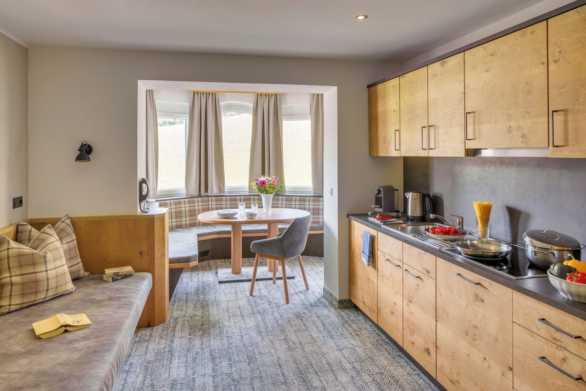 Una cocina compacta con armarios de madera, un comedor con una mesa redonda y sillas, y una zona de estar acogedora con sofá y cojines.