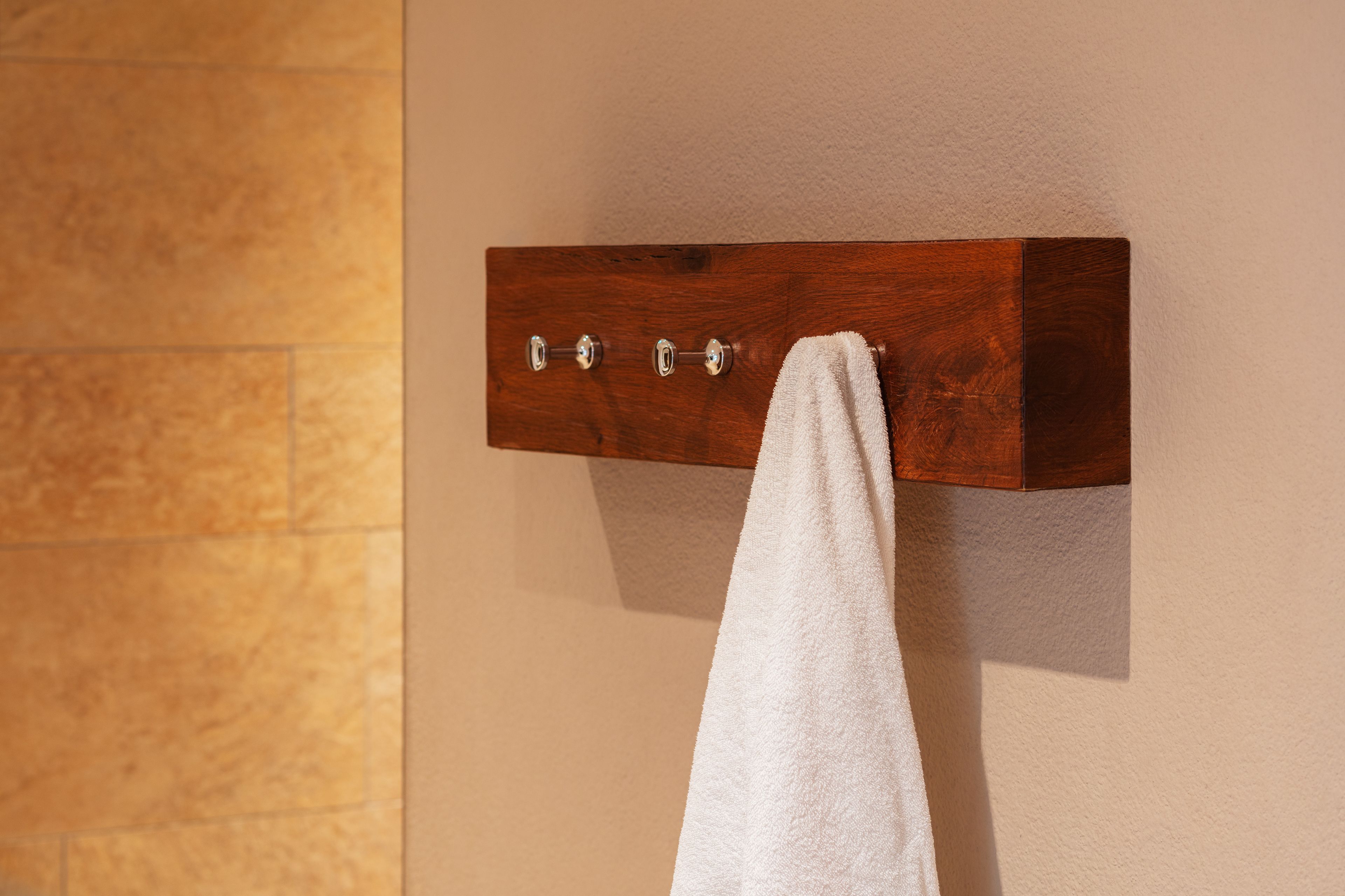 Un perchero de madera con una toalla blanca colgada, fijado en una pared color beige.