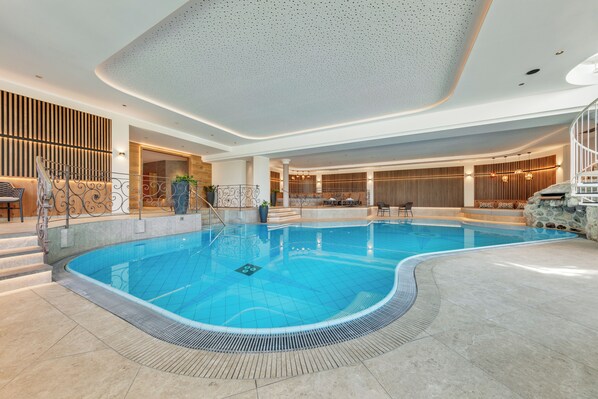 Una amplia piscina cubierta de diseño curvo, rodeada por un muro de piedra y paneles de madera.