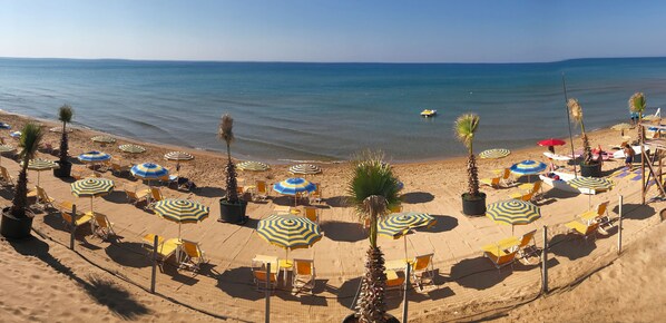 A beach with rows of sun loungers and umbrellas, a palm tree, and a clear view of the sea. - Triscinamare Hotel Residence (Castelvetrano)