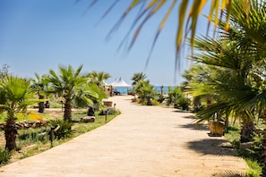 A paved pathway leading to a white tent structure, surrounded by palm trees and greenery. - Triscinamare Hotel Residence (Castelvetrano)