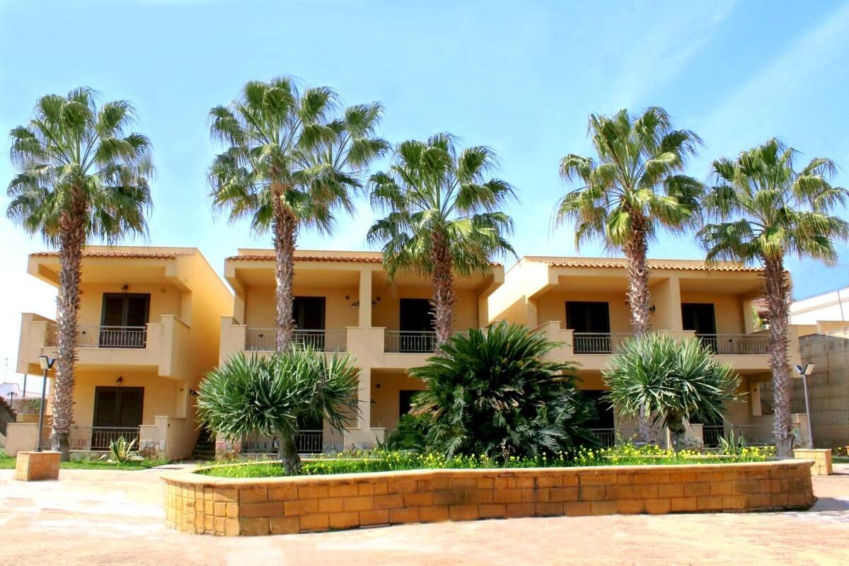 A multi-story hotel with balconies, surrounded by palm trees and a landscaped garden.