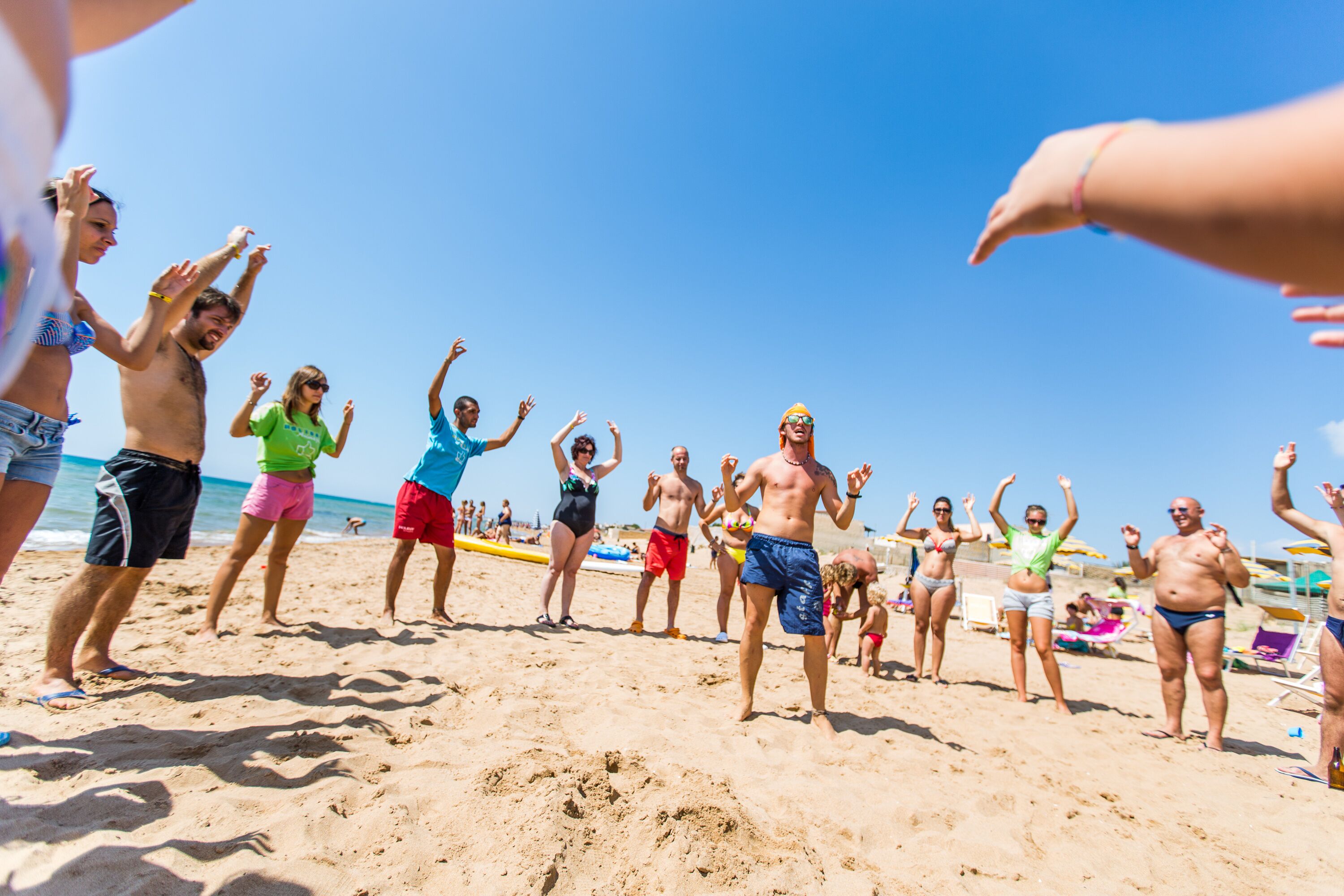 Una playa con gente de pie alzando las manos, sugiriendo un ambiente animado.