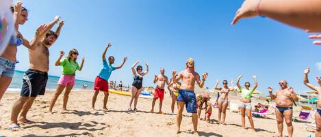 Una playa con gente de pie alzando las manos, sugiriendo un ambiente animado.