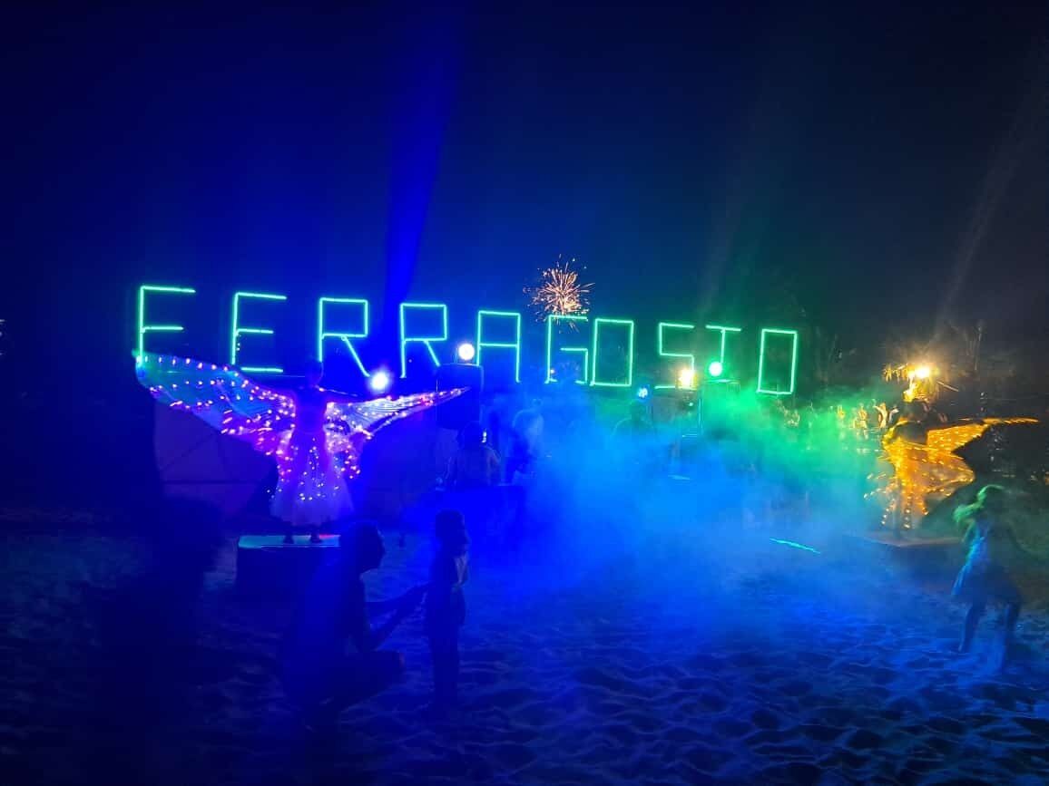 A beachside area with illuminated text spelling "FERRAGOSITO" and a decorative structure with lights.