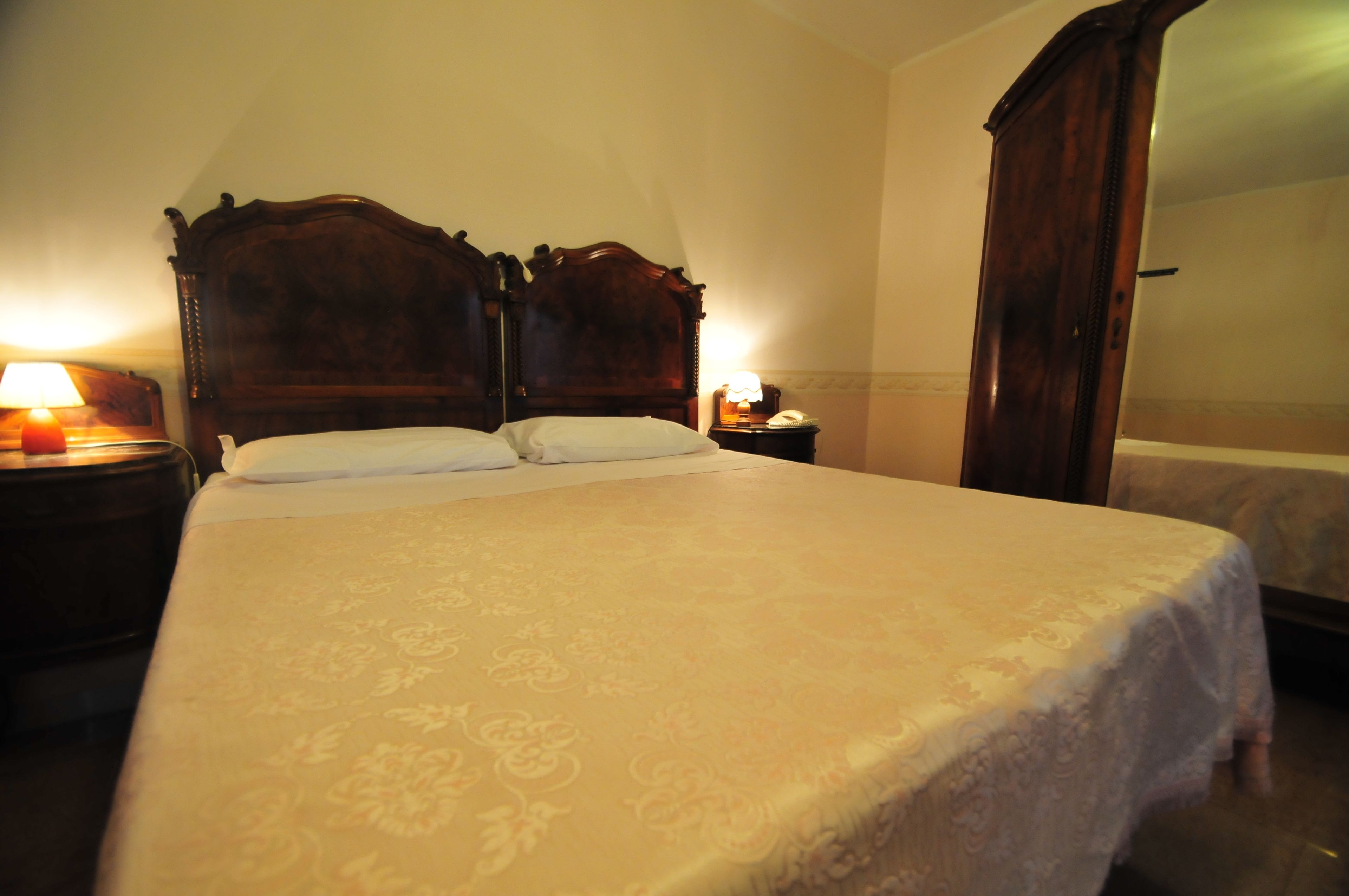 A standard hotel room with a large bed, two bedside tables with lamps, and a wardrobe.