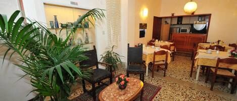 A dining area with a wooden table, chairs, and a decorative vase. There is a potted plant and a patterned rug on the floor.