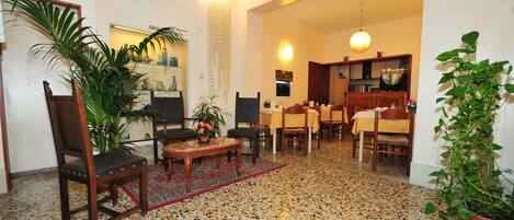 Amplia sala de estar con suelo de baldosas, una mesa de comedor con sillas, y una cocina visible a través de un vano abierto.