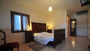 Un dormitorio con una cama de madera, una silla, una mesita de noche, una ventana con cortinas y una lámpara colgante.