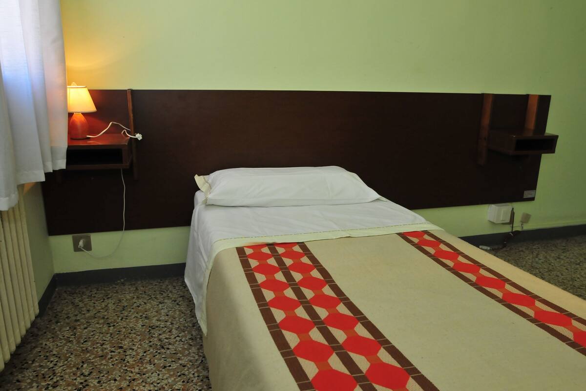 A single bed with a headboard, a bedside table with a lamp, and a patterned bedspread.