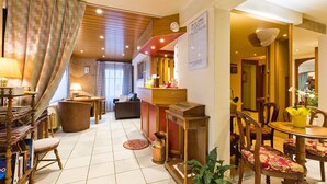 Un hall d’hôtel avec un comptoir d’accueil en bois, un espace détente avec des fauteuils et une table, et une bibliothèque remplie de livres.