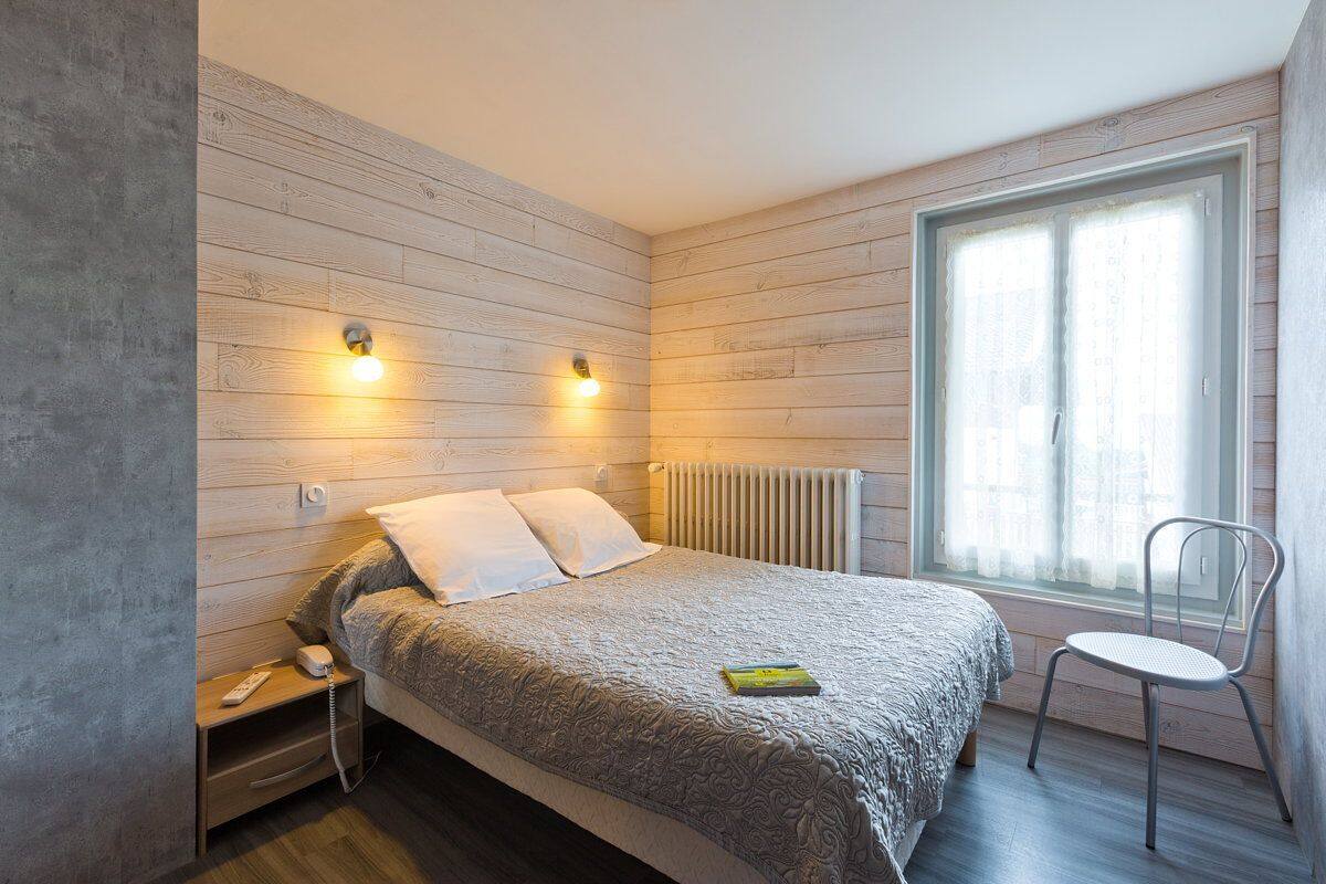 Ein Schlafzimmer mit Bett, Nachttisch, Stuhl und einem Fenster mit Vorhängen.