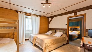 Une chambre confortable avec deux lits, un lit superposé en bois, une table avec un téléviseur et une fenêtre avec des rideaux.