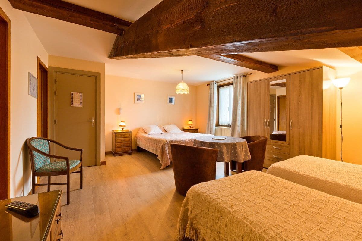 Ein Hotelzimmer mit zwei Betten, einem Schreibtisch, einem Sessel, einer Holzzahlung und einem Fenster mit Vorhängen.