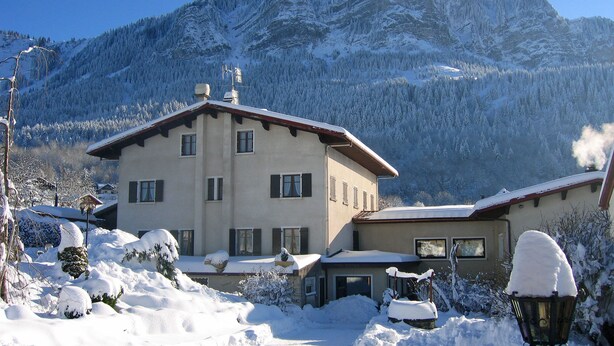Un bâtiment à deux étages, doté d’un toit en pente, entouré d’arbres et de montagnes couverts de neige.