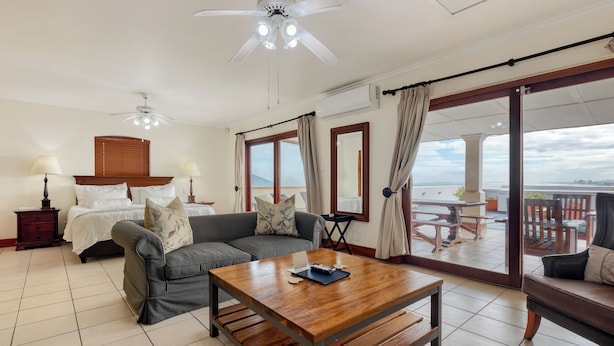 A hotel room with a bed, sofa, and a wooden coffee table. There is a balcony with a table and chairs. - Berg en Zee Guesthouse (Cape Town)