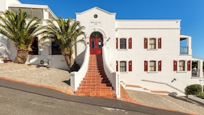 A white building with a red door and a sign reading "BERG EN ZEE 1896". - Berg en Zee Guesthouse (Cape Town)