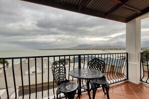 A balcony with a table and chairs overlooking a body of water and distant mountains. - Berg en Zee Guesthouse (Cape Town)