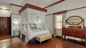 A bedroom with a four-poster bed, a wooden dresser, a bedside table with a lamp, and a window with curtains. - Berg en Zee Guesthouse (Cape Town)