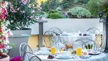 Un espace extérieur aménagé pour les repas, avec des tables dressées pour le petit-déjeuner, entouré de plantes en pot et offrant une vue sur le jardin.