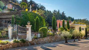 A gated entrance with a stone wall, a paved road, and a building with a red facade.