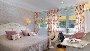 Un dormitorio con una cama grande, un escritorio y una silla. Hay una ventana con cortinas, una lámpara y un sombrero en la silla.