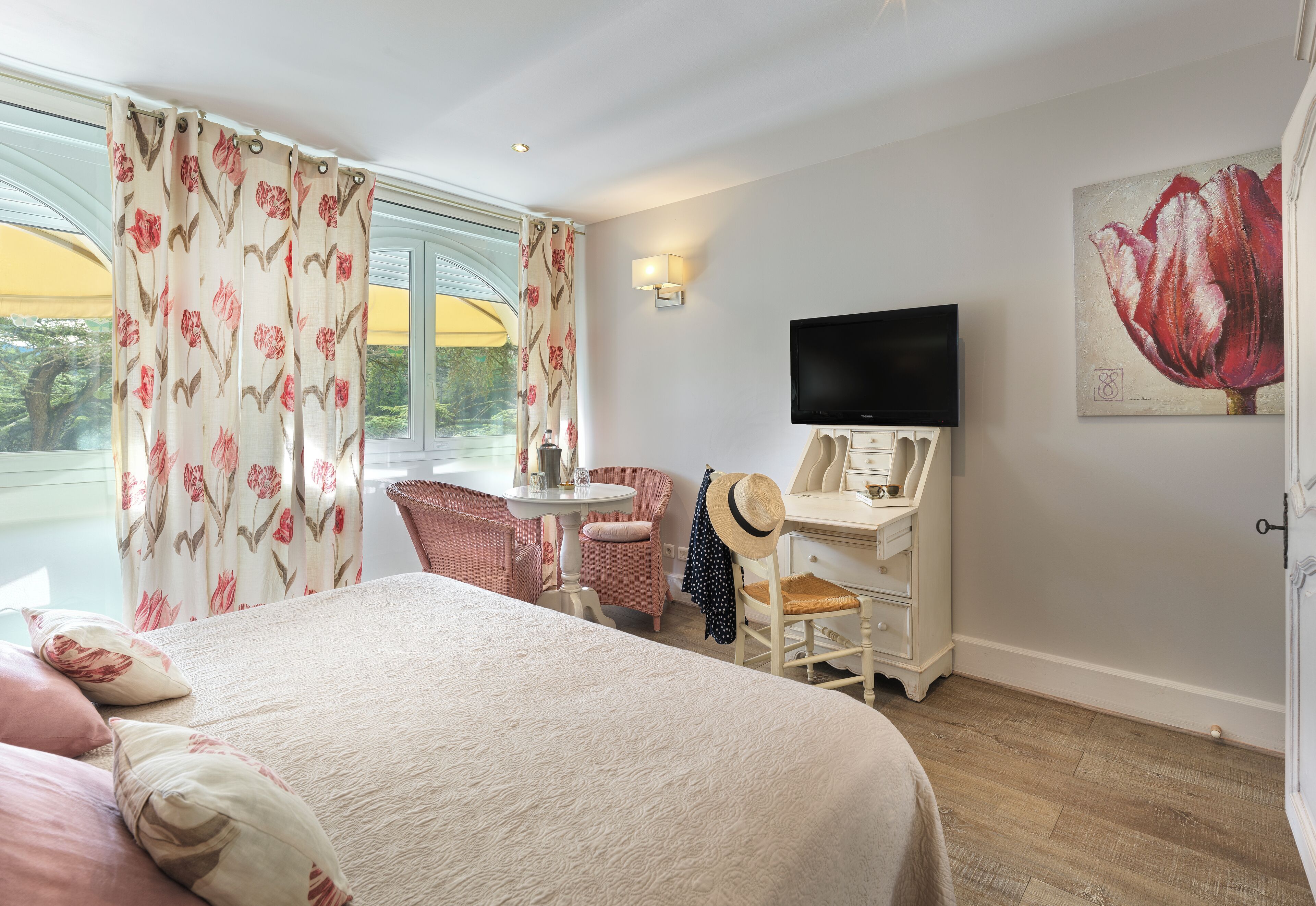A hotel room with a bed, a desk, a television, and a large window with curtains.