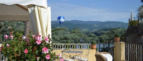 A terrace with wicker furniture, a view of the landscape, and a hot air balloon in the distance.