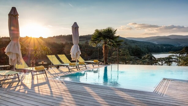 Zona junto a la piscina con sillones de descanso y sombrillas, con vistas a un paisaje pintoresco que incluye montañas y una masa de agua.