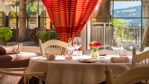 Una mesa de comedor con copas de vino, un florero con flores y vistas a un jardín y montañas a través de grandes ventanales.