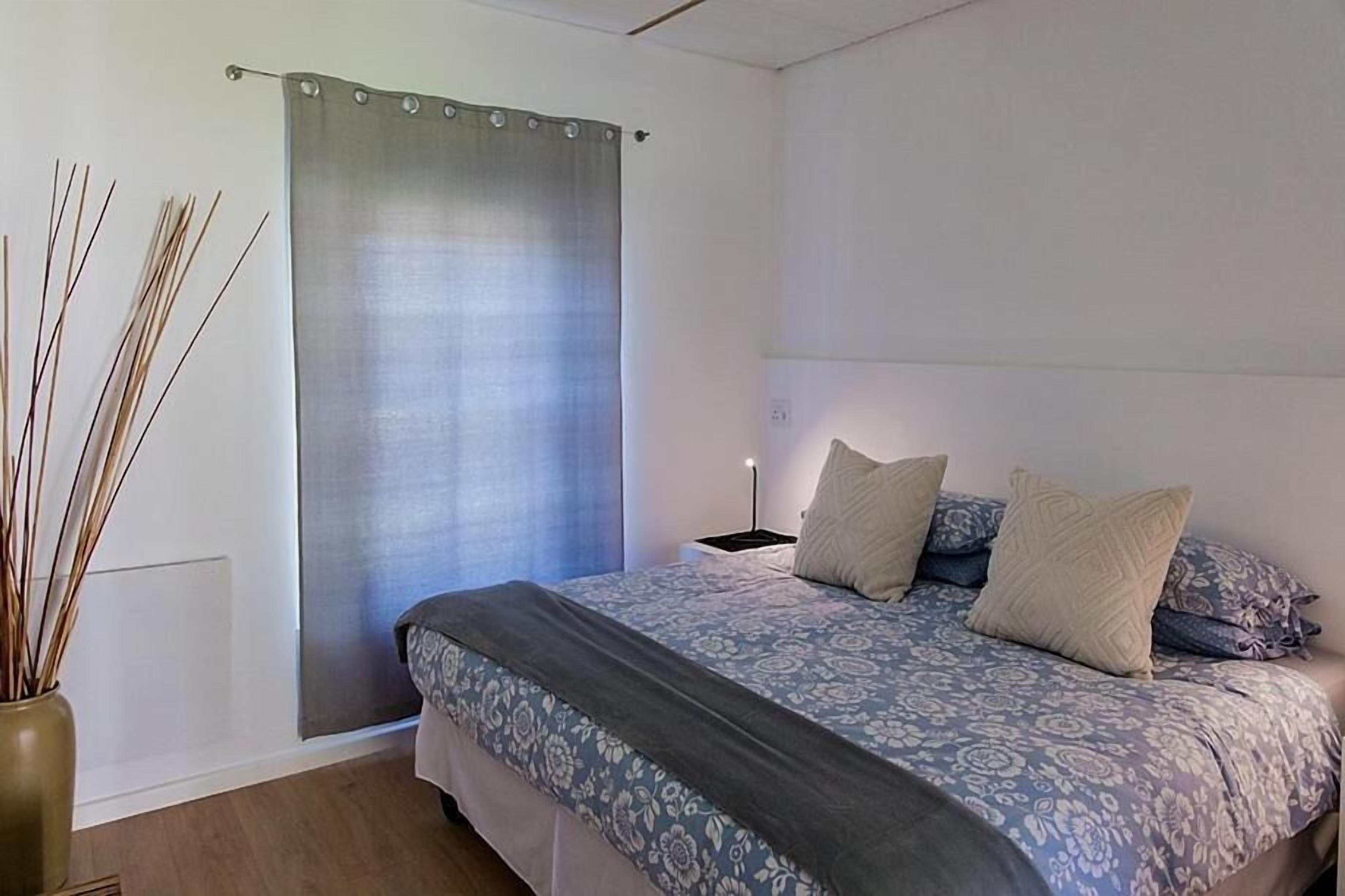 Une chambre à coucher avec un lit, une table de chevet, une lampe et un rideau.