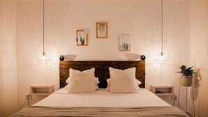 A bedroom with a large bed, two bedside tables, and a wooden headboard. There are two wall-mounted lamps and three framed pictures on the wall. - La Sosta Restaurant & Guest House (Swellendam)