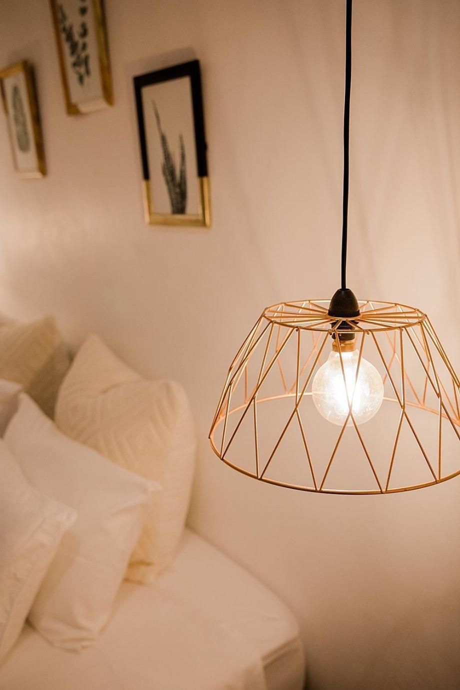 A room with a bed, a hanging light fixture, and framed artwork on the wall.