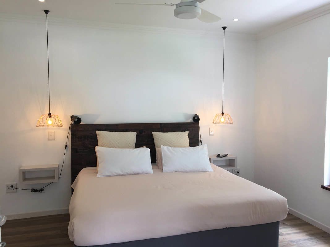 A modern bedroom with a large bed, two bedside tables, and pendant lights.