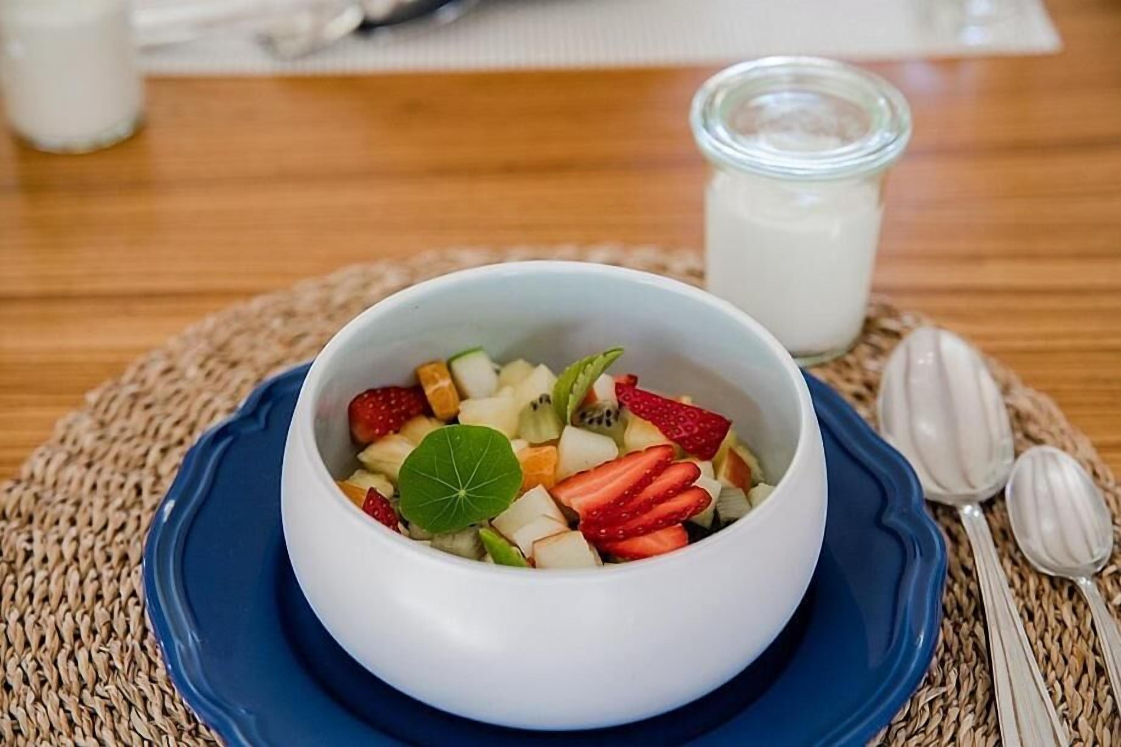 A bowl of fruit salad on a blue plate with a woven placemat underneath.