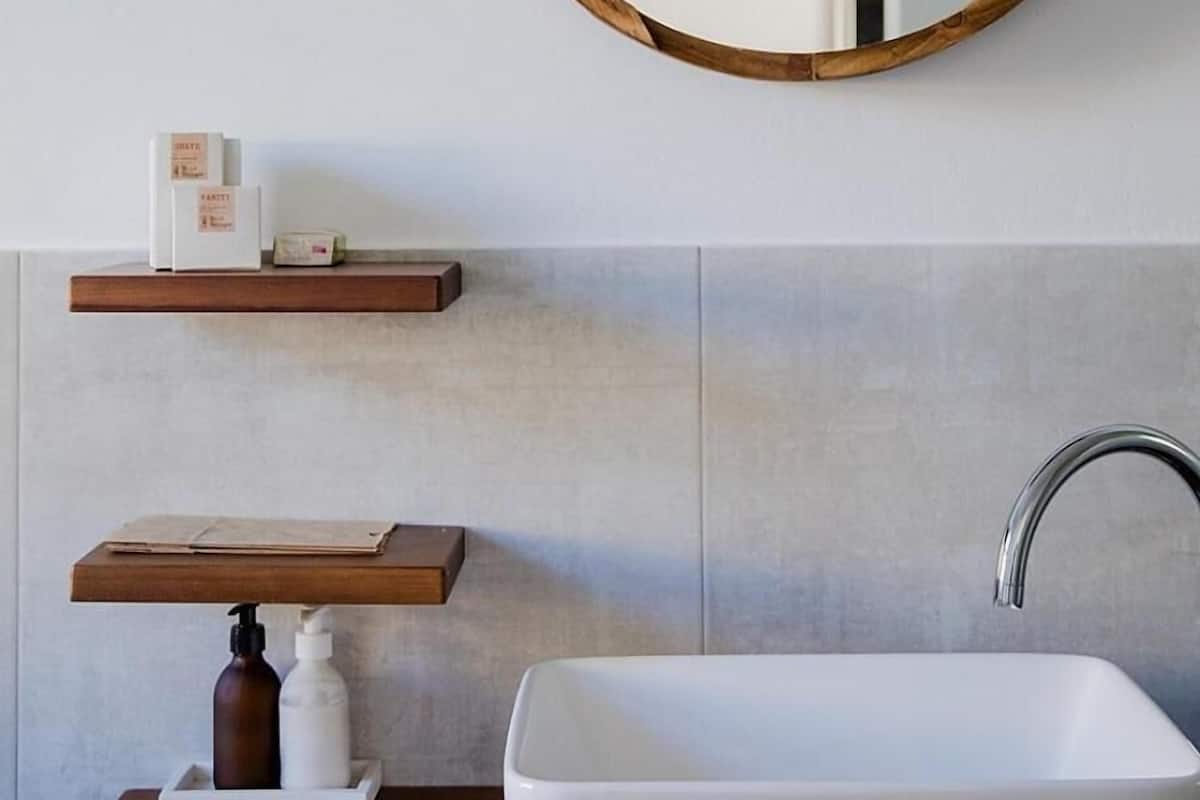 A bathroom with a white sink, a wooden-framed mirror, and two wooden shelves with toiletries.