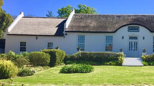 A white building with a thatched roof, a central entrance with steps, and a small garden with hedges and plants. - La Sosta Restaurant & Guest House (Swellendam)