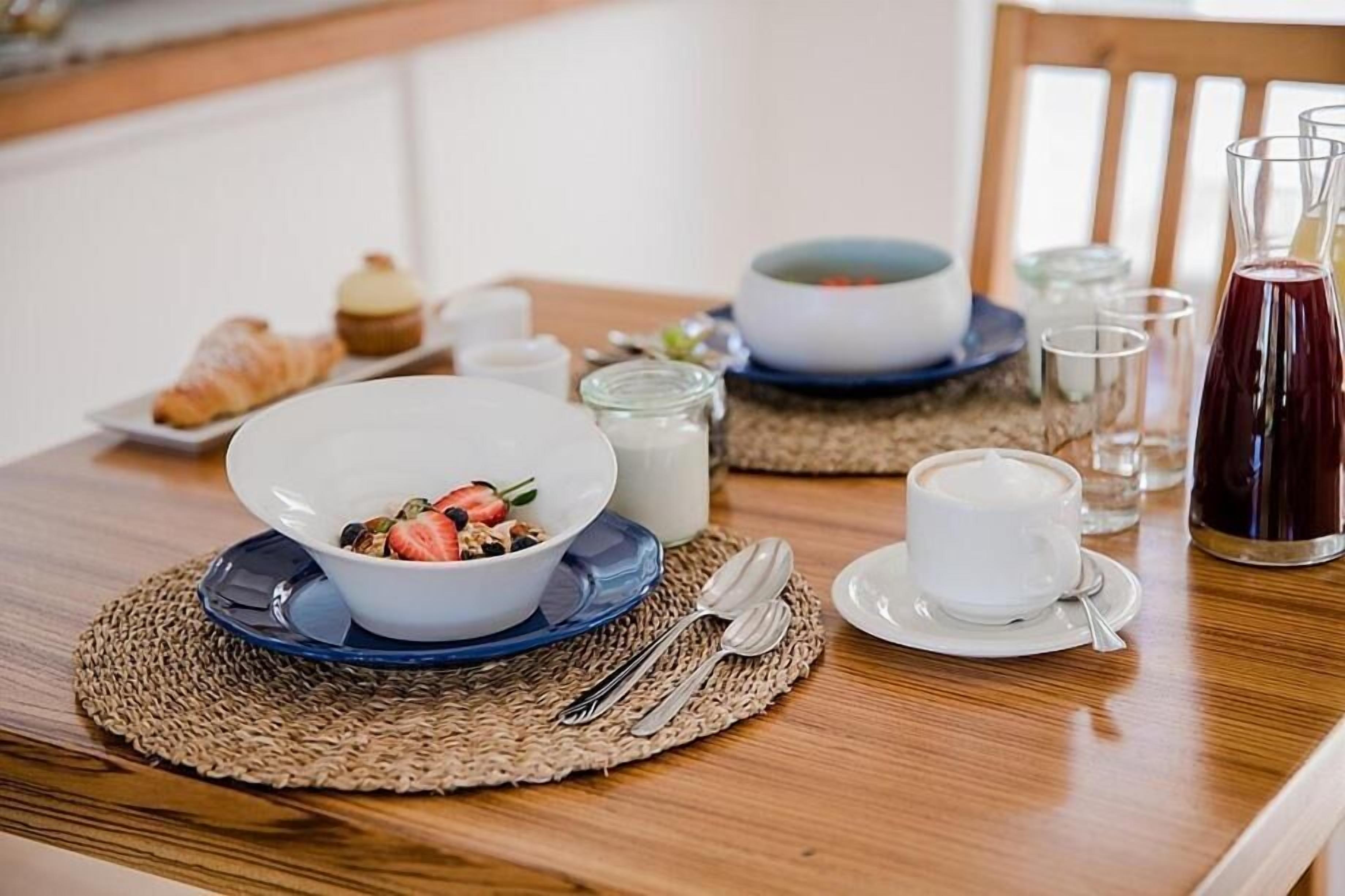 A breakfast setting with a bowl of cereal, a croissant, a cup of coffee, and a glass of juice on a wooden table.