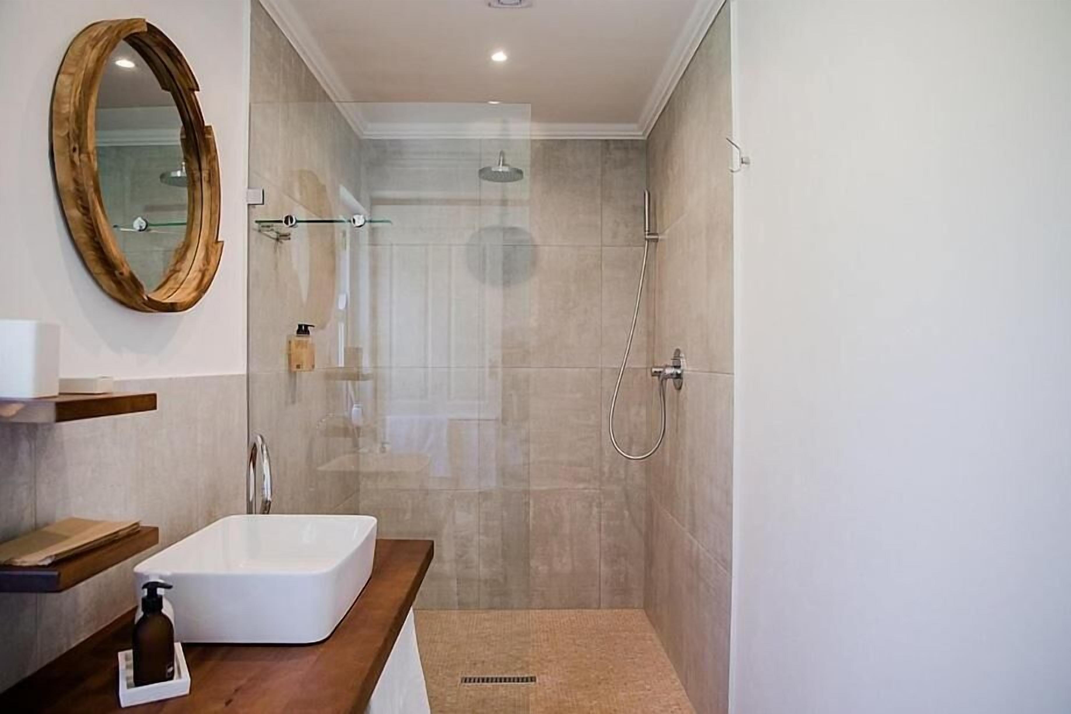 Een moderne badkamer met een douchecabine van glas, een witte wastafel en een houten opbergmeubel.