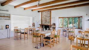 A dining area with wooden tables and chairs, a stone fireplace, and large windows with a view of greenery. - La Sosta Restaurant & Guest House (Swellendam)
