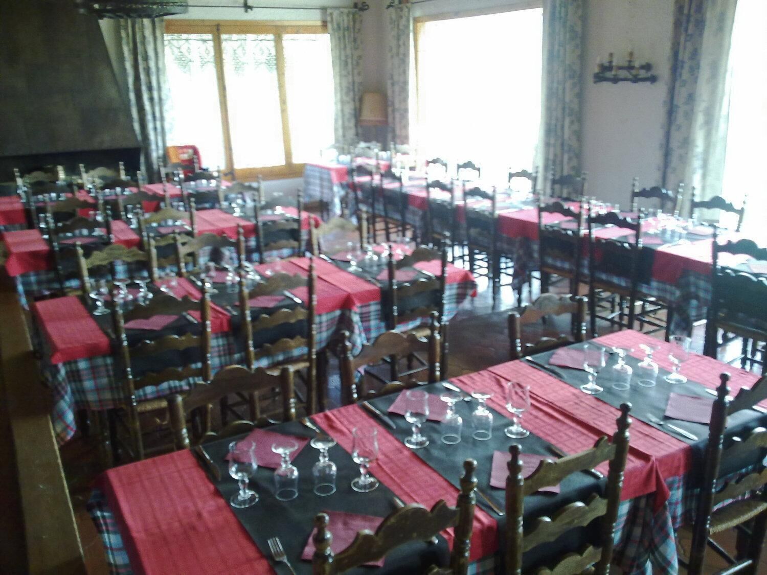 A dining area with multiple tables set for service, each with a red tablecloth and silverware.
